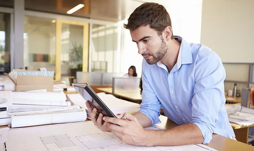Profesional con tableta revisando planos en la oficina, usando apps para PYMES