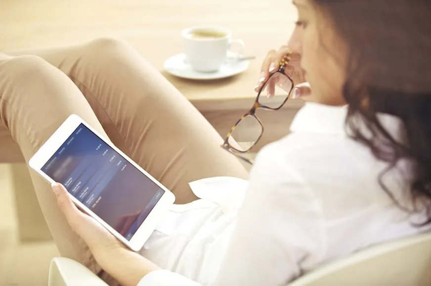 Mujer con tableta y café revisando una aplicación, reflejando el uso cotidiano de apps imprescindibles para PYMEs