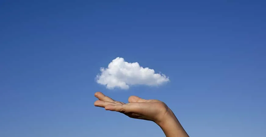 Mano sosteniendo una nube blanca sobre cielo azul, metáfora del cloud computing
