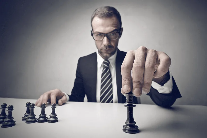 Comercial con gafas y traje moviendo pieza de ajedrez, estrategia de ventas