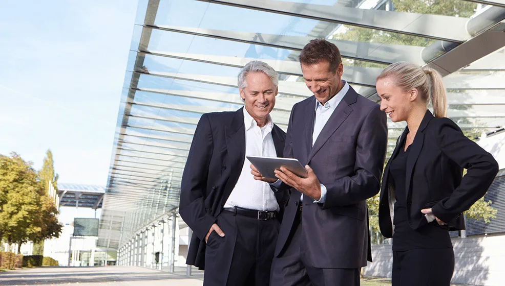 Tres comerciales de distintas edades revisando una tablet frente a edificio moderno