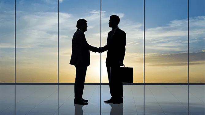 Dos empresarios estrechando manos al cerrar una venta en una oficina al atardecer