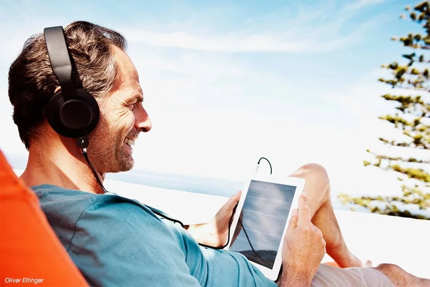 Hombre leyendo un ebook en tablet con auriculares durante las vacaciones al aire libre