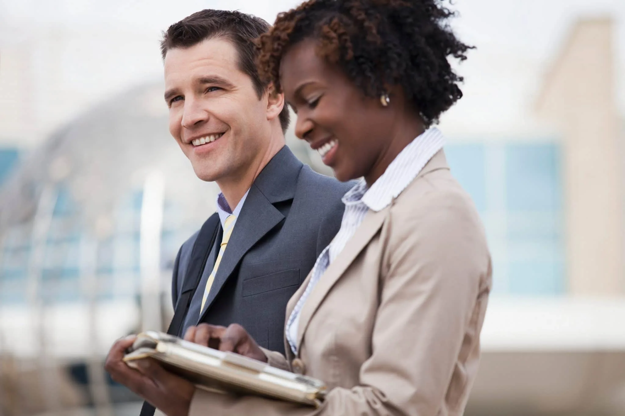 Dos ejecutivos sonriendo mientras consultan una tablet, ejemplo de movilidad empresarial