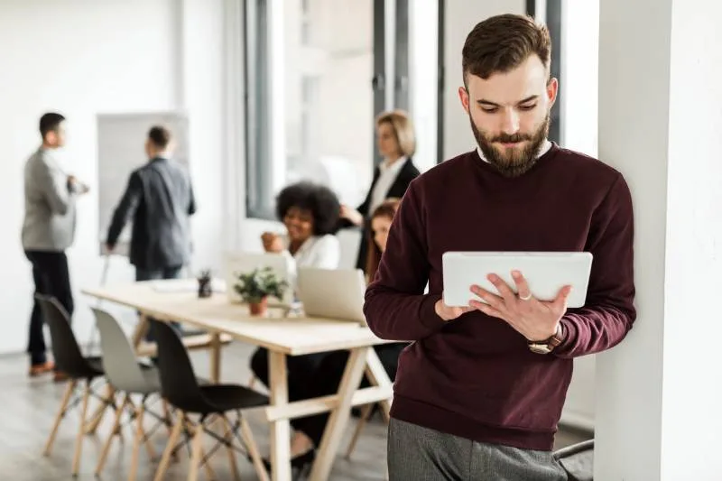 Profesional usando un iPad en la oficina con compañeros reunidos al fondo