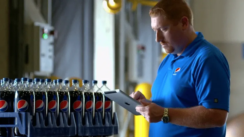 Empleado de Pepsi usando iPad junto a botellas en planta de distribución