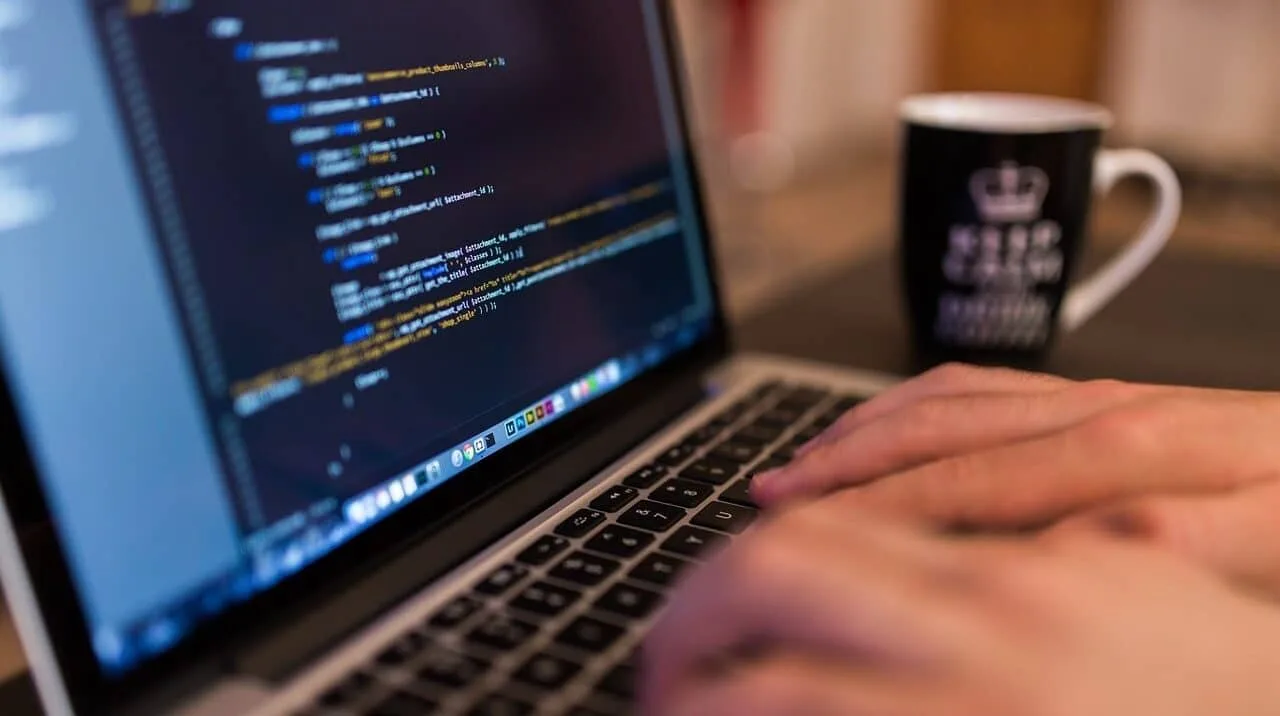 Programador escribiendo código en portátil durante proceso de desarrollo de software a medida