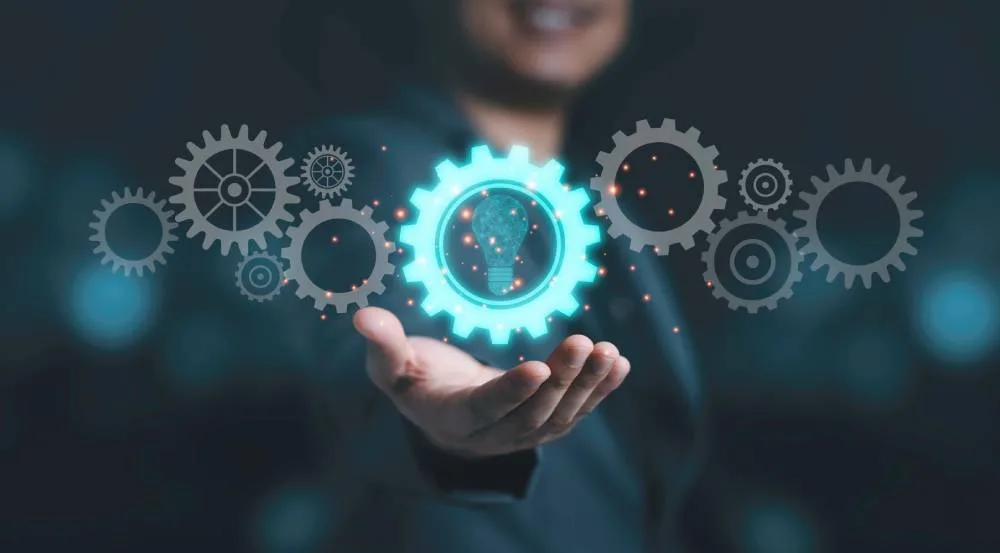 Mano sosteniendo engranajes y bombilla que representan soporte y mantenimiento continuo de software