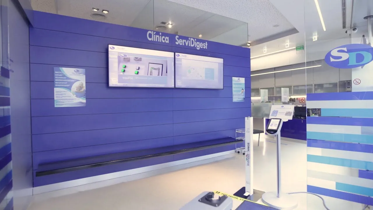 Recepción de la Clínica Servidigest con pantallas informativas y mobiliario corporativo en tonos azules